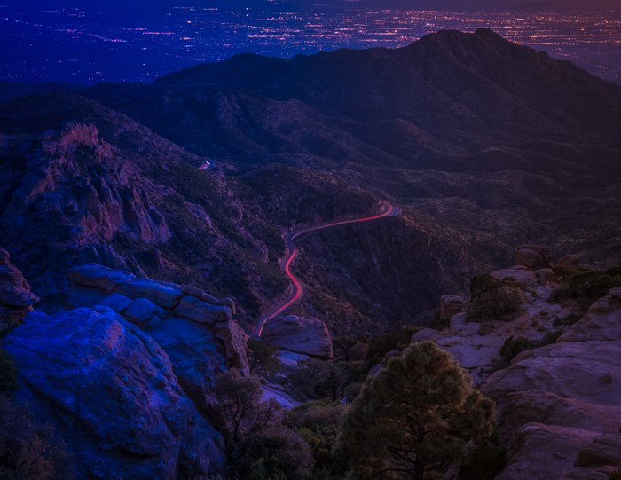 Mountain range with winding road and city lights at dusk