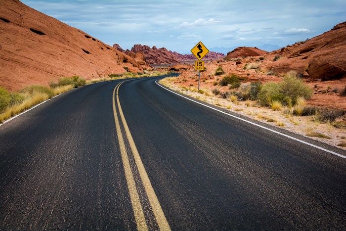 Desert highway with winding road and road sign