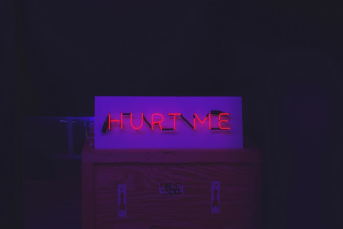 Neon sign that says "HURT ME" on a wooden box