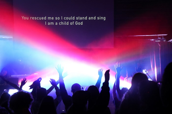 Crowd with hands raised at a concert with lyrics on screen
