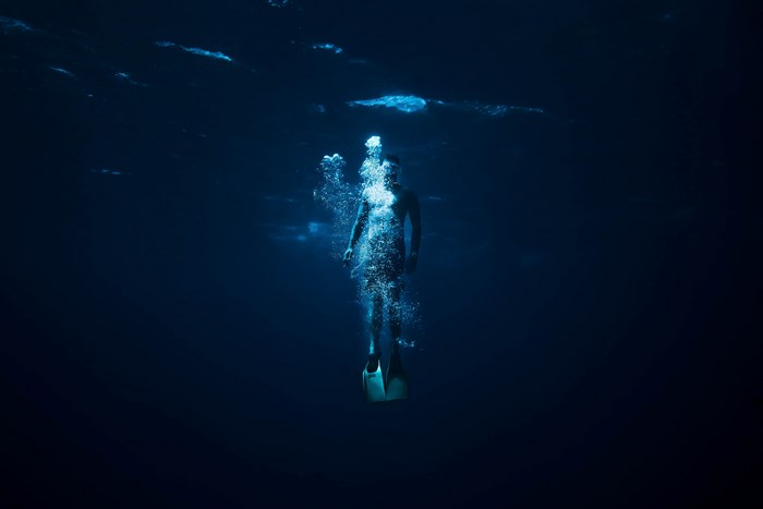 Person free diving underwater with bubbles and fins