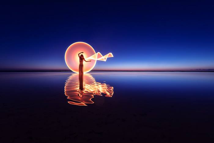 Woman with light painting reflection on lake at dusk