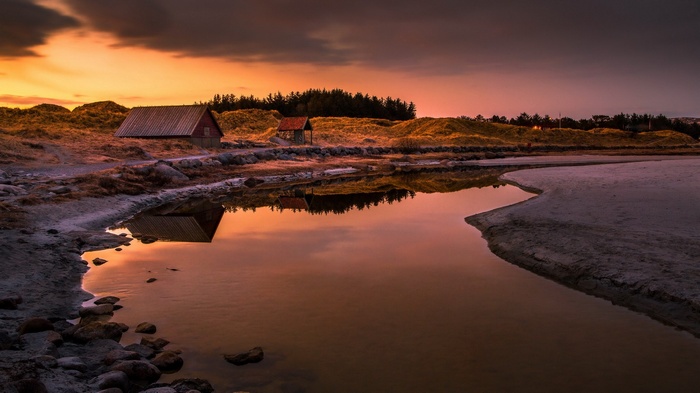 Two small cabins by a calm body of water at sunset