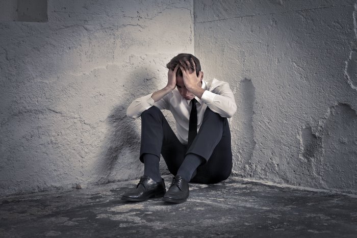 Man sitting in a corner with head in hands