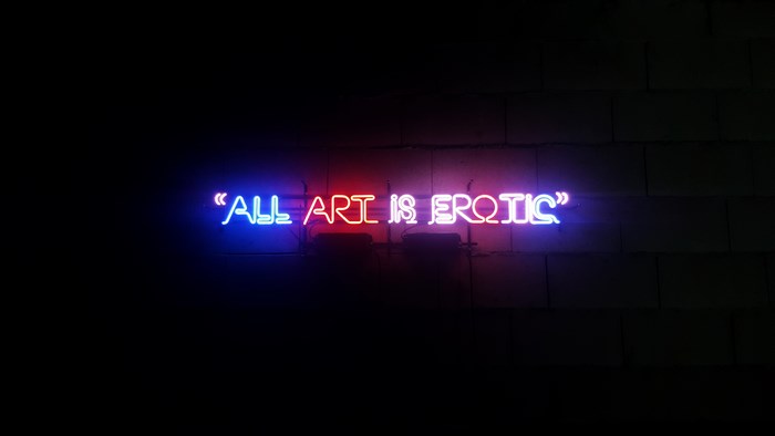 Neon sign "All Art is Erotic" on a brick wall