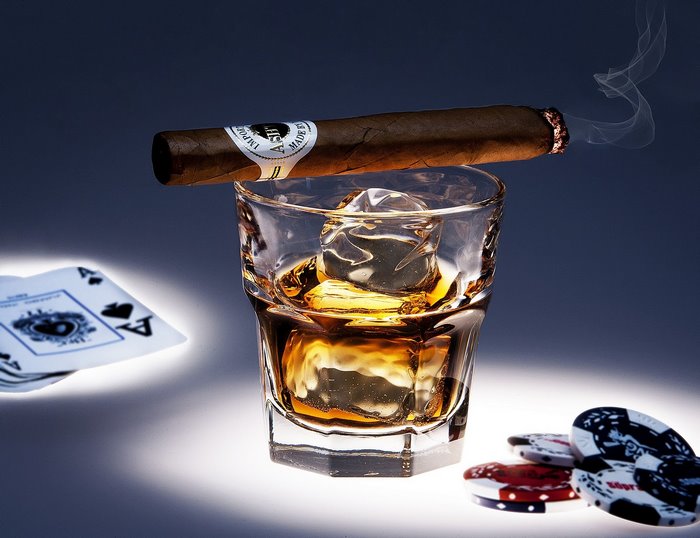 Cigar resting on a glass of whiskey with playing cards and poker chips