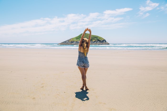 Woman stretching on a sandy beach with an island in the background