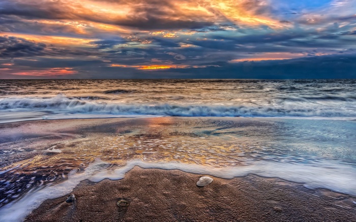 Sunset over the ocean with waves crashing on the beach