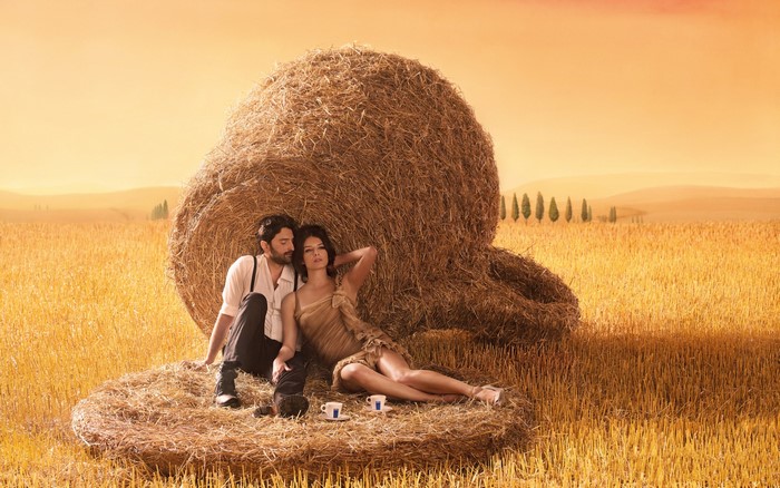 Couple relaxing by hay bales in a wheat field