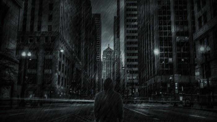Person in hoodie standing in rainy city street at night