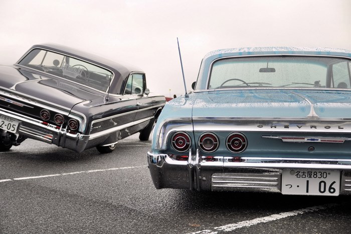Two classic Chevrolet lowriders parked on a wet asphalt lot
