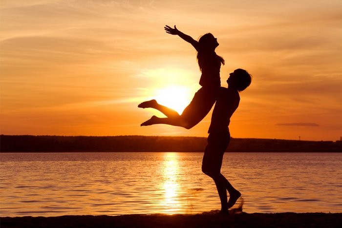 Couple silhouetted against a sunset over the sea