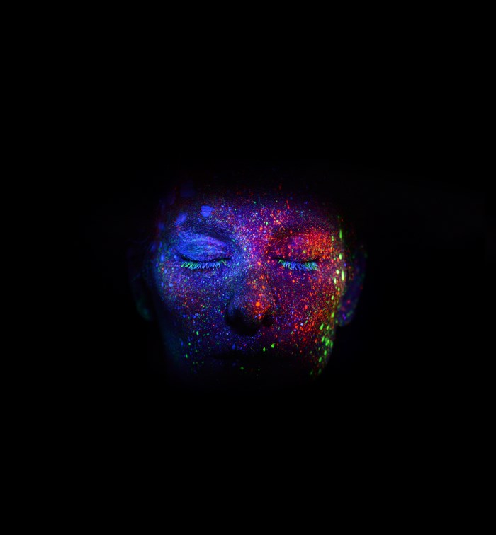 Face covered in colorful UV paint with eyes closed