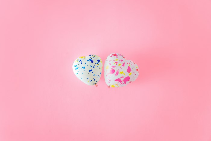 Two heart-shaped balloons with paint splatters on pink background