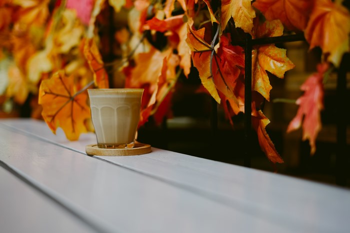 Latte in glass on wooden coaster with autumn leaves