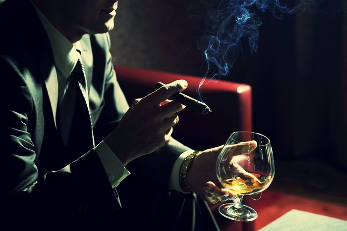 Man in suit smoking cigar and drinking whiskey
