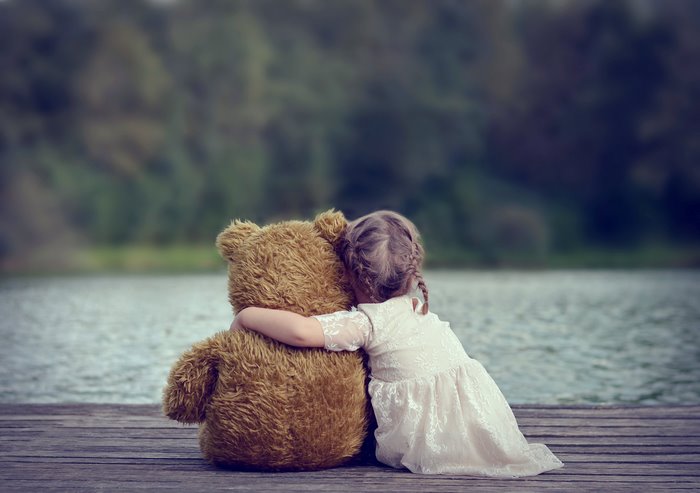Girl hugging a teddy bear by a lake