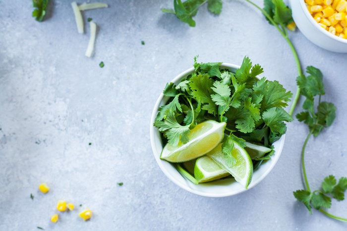 Cilantro and lime wedges in a bowl with corn