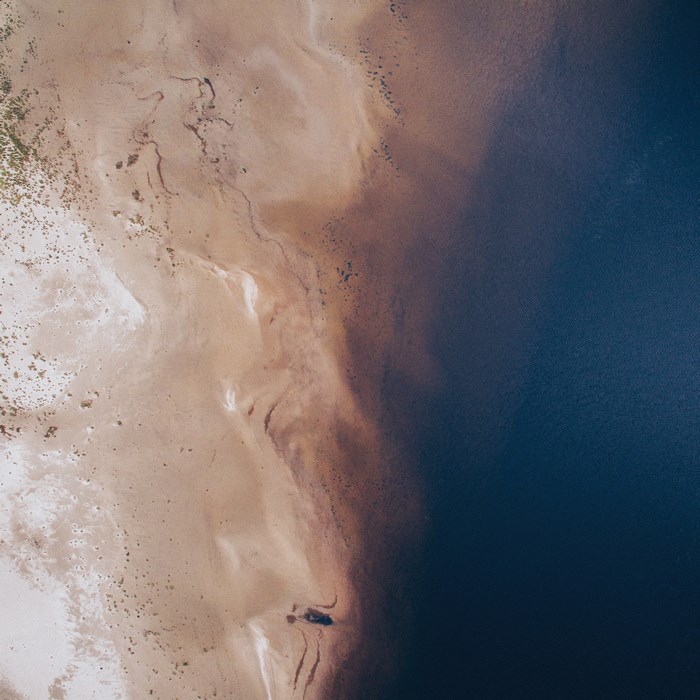 Aerial view of sandy shore meeting dark blue water
