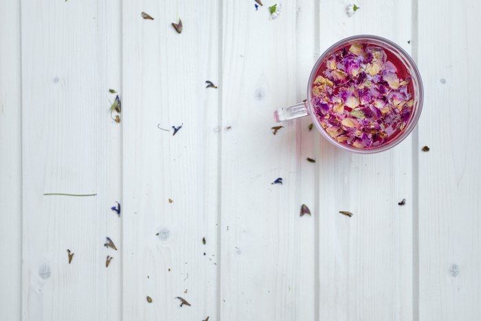 Floral tea with rose petals in a glass cup on a white wooden table
