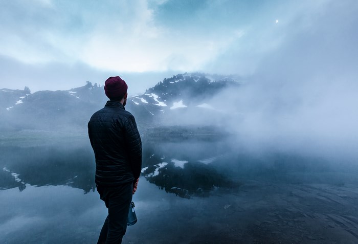 Man in hat looking at misty mountains and lake