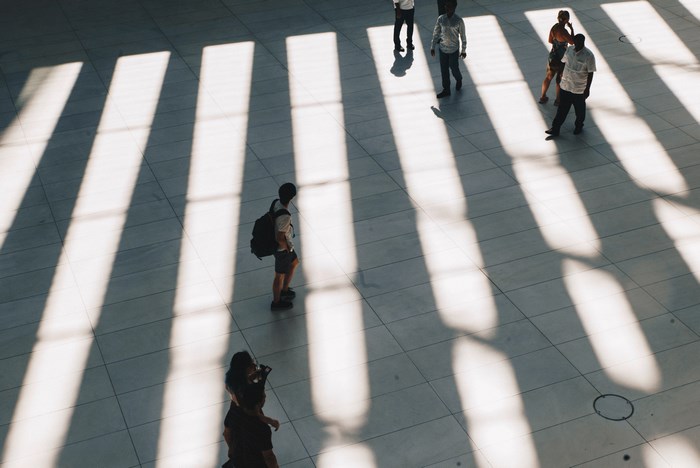 People walking in a sunlit hall with striped shadows