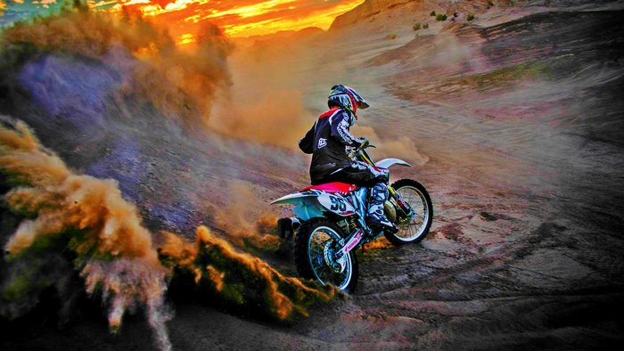 Motocross rider kicking up dust at sunset