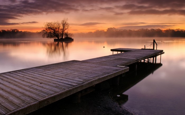 Wooden pier on a lake at sunrise with mist
