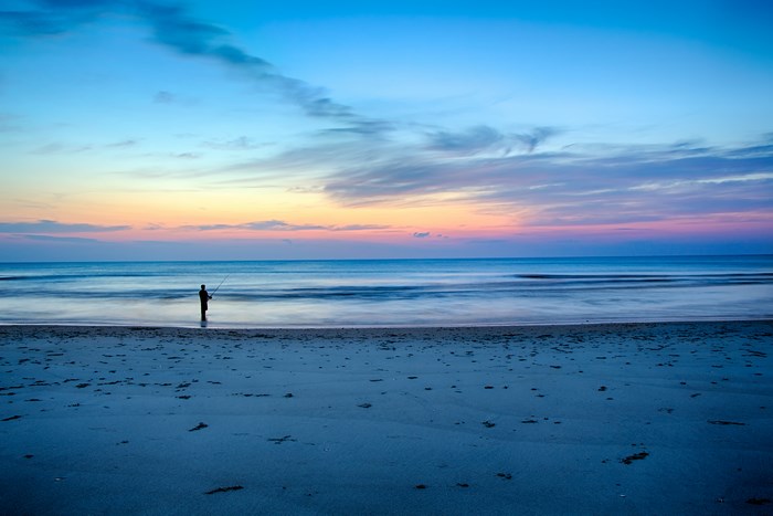 Fisherman silhouetted against a colorful twilight sky over the ocean