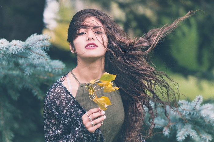 Woman holding yellow leaves with wind blowing her hair