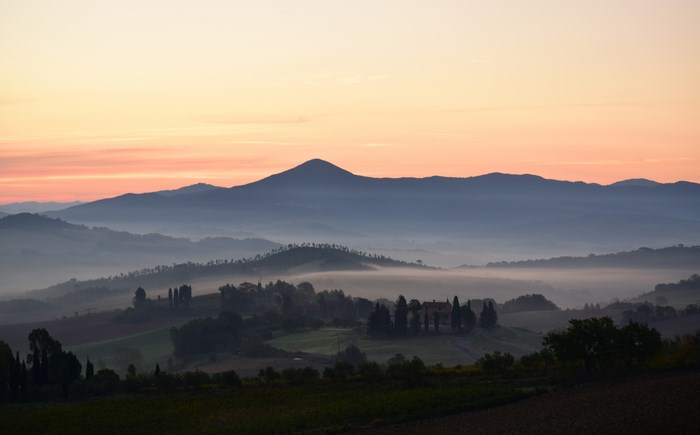 Misty Tuscan hills at sunrise with a prominent mountain peak