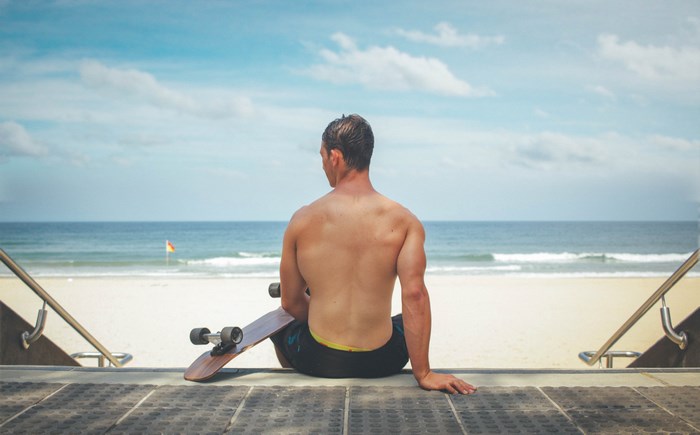 Man with skateboard sitting on stairs at the beach