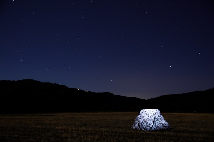 Tent glowing under a starry night sky with mountains