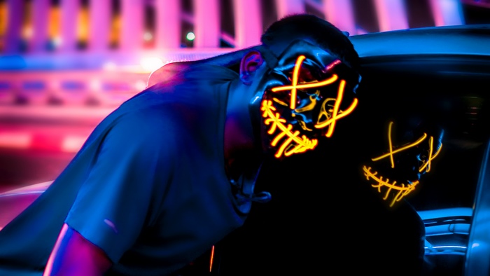 Man wearing a neon purge mask in a car at night