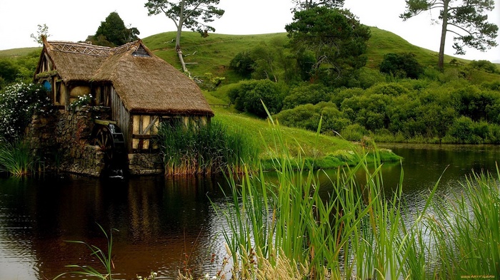 Hobbiton watermill by a lake with rolling hills
