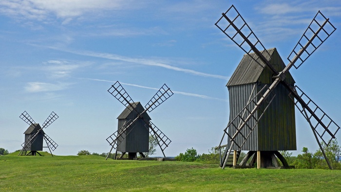 Three wooden windmills on a grassy hill under a blue sky