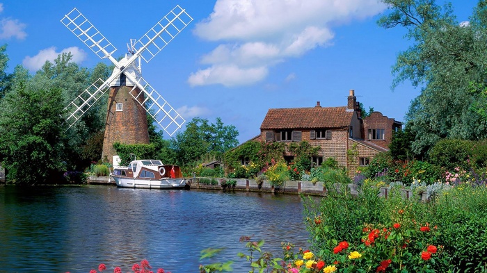 Windmill and house by a river with a boat