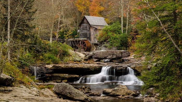 Old wooden mill with water wheel by waterfall in autumn forest