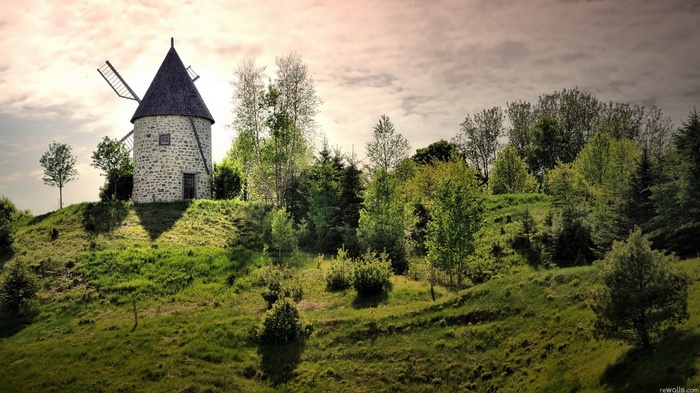 Stone windmill on a grassy hill with trees