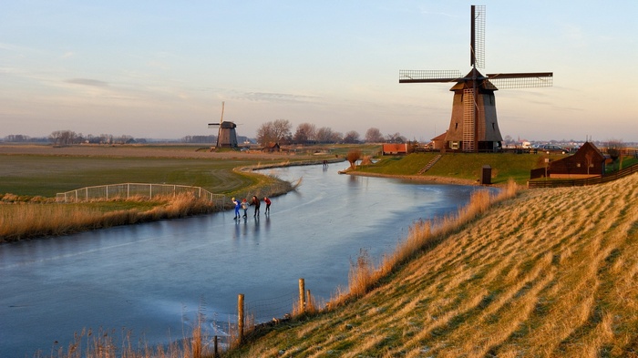 People ice skating near windmills at sunset