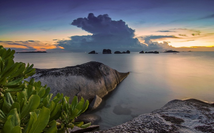 Rocky beach at sunset with calm sea and dramatic clouds