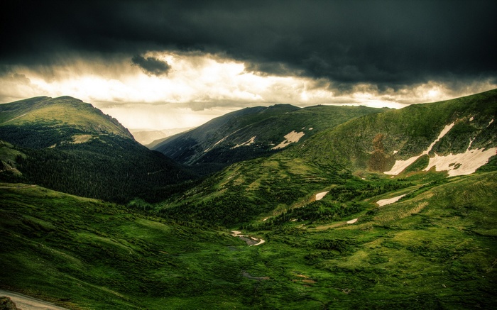 Stormy sky over green mountains with patches of snow