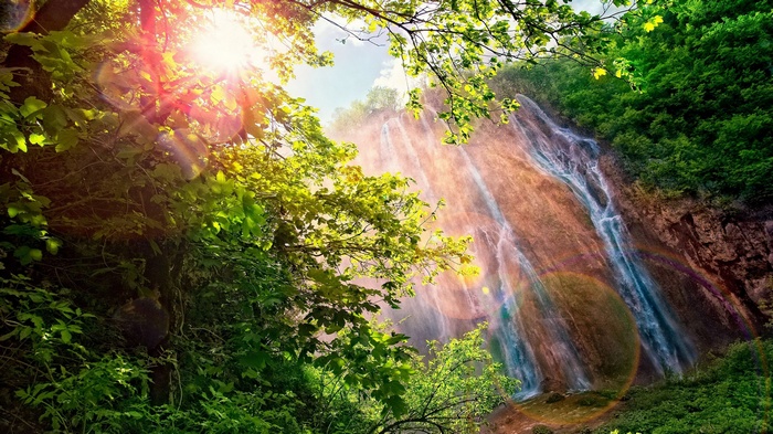 Sunlight streams through trees onto a cascading waterfall