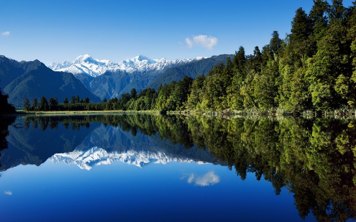 Snow-capped mountains reflected in a calm lake with a forest