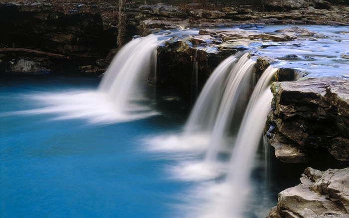 Waterfalls cascading over rocks into a blue pool