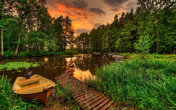 Boats docked by a wooden pier on a lake at sunset