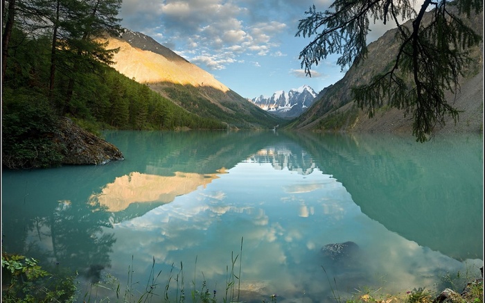 Turquoise mountain lake reflecting snow-capped peaks and clouds