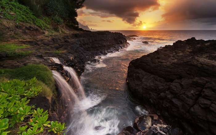 Waterfall cascading into the ocean at sunset