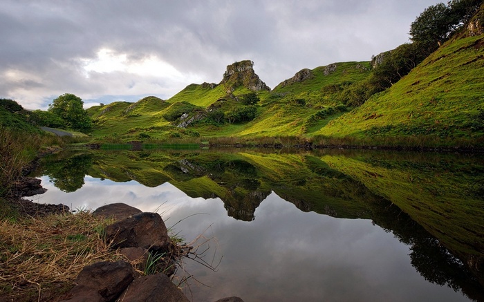 Green hills reflected in a calm lake under a cloudy sky