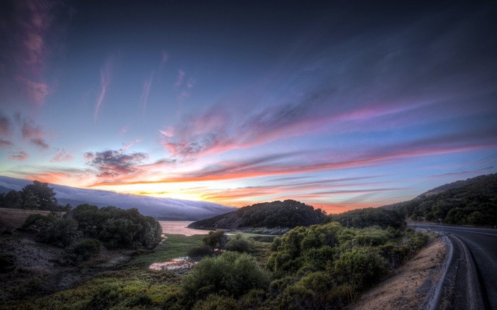 Road curving through hills at sunset with colorful sky